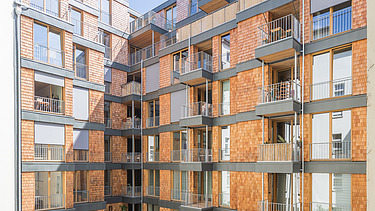 Foto einer mehrgeschossigen Wohnanlage aus Holz. Man sieht einen Detailausschnitt der Fassade aus Holzschindeln.