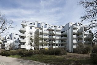 Photo of a multi-storey building with a white façade. Wooden extension.