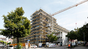 Photo of the VINZENT building shell in Munich. You can see a scaffolded, multi-storey building.