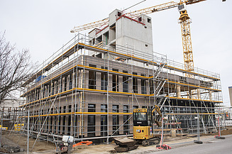 Foto des Rohbaus von Außen des Büroneubaus T3 in Aichach. Man sieht ein eingerüstetes Holzgebäude.