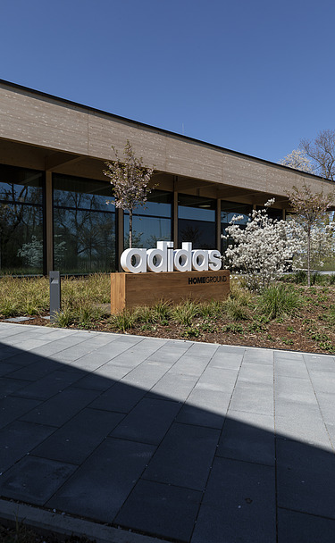 Homeground adidas Herzogenaurach Photo of a building with a flat roof. In front of it is a sign with the inscription adidas