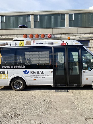 Foto vom BG BAU-Bus. Er ist weiß und hat Aufschriften drauf.