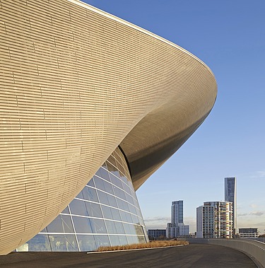 Photo of the Aquatics Center in London from the inside. You can see the wooden roof construction and a large swimming pool.