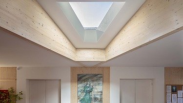 Photo of an interior with wooden ceiling and triangular window. A picture hangs on the wall.