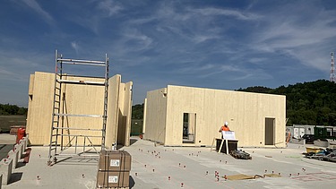 Baustellenfoto, auf dem die Montage der ersten Brettsperrholzelemente zu sehen ist.