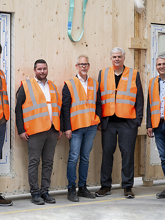 Five men standing in front of a wooden element in the ZÜBLIN Timber production hall.