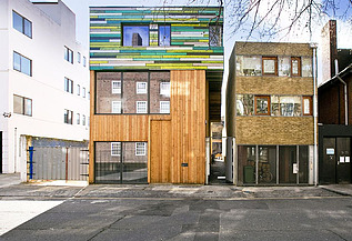 Nachverdichtung WoodBlock House London Foto mehrerer Gebäude. In der Mitte ist ein neuer Holzbau mit bunter Fassade im oberen Teil zu sehen.