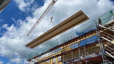 Photo of a timber construction site in Berlin. You can see an overlong ribbed element on the crane.