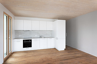 Foto eines möblierten Wohnraumes, des Holzgebäudes CARL in Pforzheim. Man sieht eine weiße Küche.