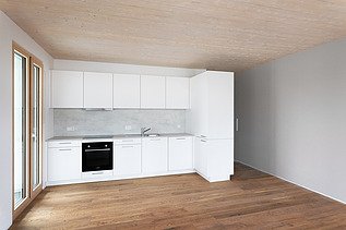 Photo of a furnished living room in the CARL wooden building in Pforzheim. You can see a white kitchen.