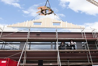 Photo of a wooden gable wall element suspended from a crane above the Schule am Hangs in Frankfurt.