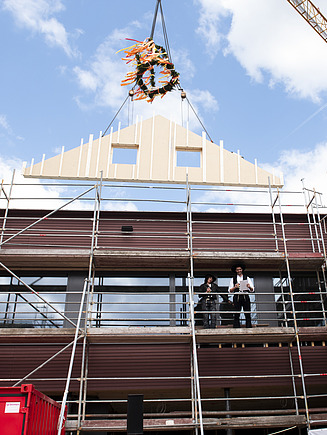 Photo of a wooden gable wall element suspended from a crane above the Schule am Hangs in Frankfurt.