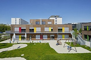 Foto eines Kindergartens in München. Zu sehen ist ein Gebäude aus Holz mit Garten.