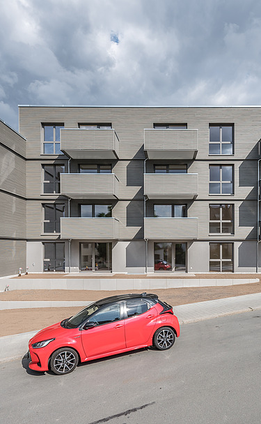 Joseph-Stiftung, Bayreuth MOLENO Foto der Joseph-Stiftung in Bayreuth. Man sieht ein Gebäude mit grauer Fassade und ein vorbeifahrendes, rotes Auto.