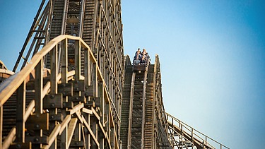 Foto der Holzachterbahn Colossos im Heide Park Resort Soltau. Zu sehen ist ein Teil der Achterbahn und ein Wagon mit Menschen.