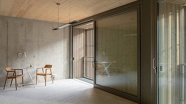 Foto der mehrgeschossigen Wohnanlage in der Stendaler Straße Berlin. Man sieht einen leeren Raum mit Holzdecke und Holzstühlen.