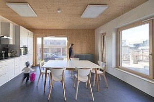 Interior shot of a furnished kitchen. You can see lots of wooden surfaces and large windows.