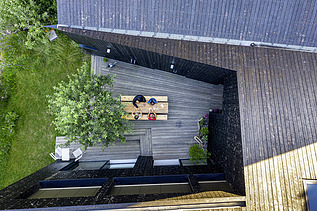 Foto eines Wohnhauses aus Holz und mit dunkler Holzfassade. Blick von oben auf die Terrasse.