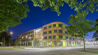 Photo of an exterior shot at night. You can see an illuminated large wooden building with a wooden façade and green façade elements.