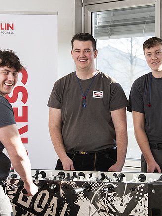 Photo of young carpenters standing around a table football and laughing.