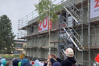 Aktuelles ZÜBLIN Timber. Schule Emleben beim Richtfest. Foto vom Richtfest Schule Emleben mit Kindern und Menschen vor dem MOLENO-Gebäude. Der Richtbaum wird gerade hochgezogen.
