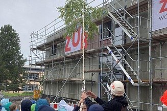 Foto vom Richtfest Schule Emleben mit Kindern und Menschen vor dem MOLENO-Gebäude. Der Richtbaum wird gerade hochgezogen.