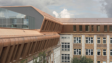 Photo of an aerial view of a multi-storey building. Metropolitan School Berlin. The wooden extension has a bronze sheet metal cladding.