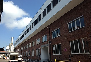 Photo of a multi-storey building. Wooden extension with white façade and flat roof.