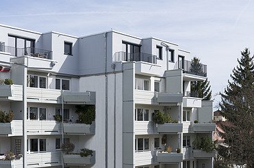 Foto eines mehrgeschossigen Gebäudes mit weißer Fassade. Aufstockung aus Holz.