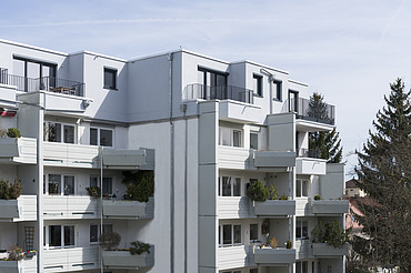 Photo of a multi-storey building with a white façade. Wooden extension.