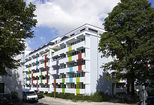 Aufstockung Bodenehrstraße München Foto eines mehrgeschossigen Gebäudes mit weiß-bunter Fassade.