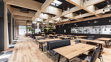 Foto eines Aufenthaltraumes mit Holztischen und Stühlen. Holzboden und Holzdecke.