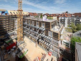 Foto des Rohbaus VINZENT in München. Zu sehen ist ein eingerüstetes, mehrgeschossiges Gebäude.