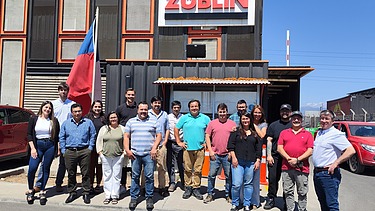 Photo of a group of 17 people. A building with a large ZÜBLIN logo and blue sky can be seen in the background