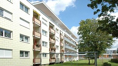 Photo of a multi-storey building with garden in front. Wooden extension.