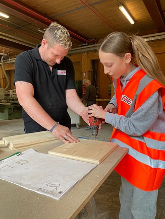 Photo of a man and a girl working with a cordless screwdriver and wood.