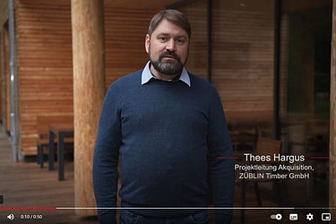 Photo of a man standing in front of a wooden building.