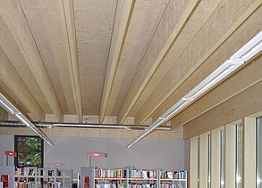 Foto einer Bibliothek von innen. Das Augenmerk liegt hauptsächlich auf der Rippendecke aus Holz.