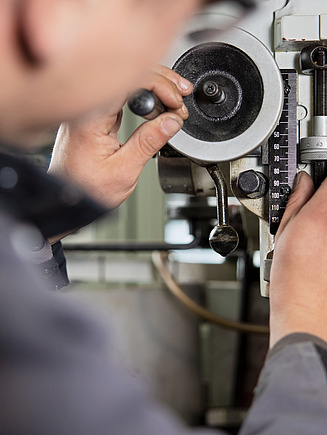 Foto einer angeschnittenen männlichen Person von hinten, die an einer Maschine steht.
