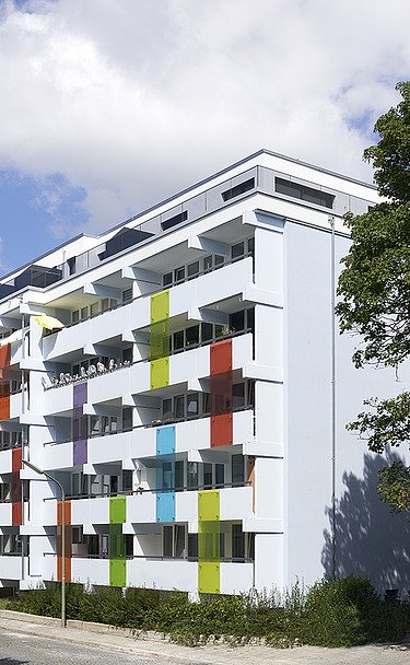 Aufstockung Bodenehrstraße München Foto eines mehrgeschossigen Gebäudes mit weiß-bunter Fassade.