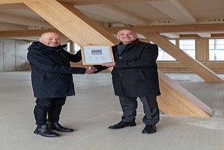 Foto von zwei Personen im neuen UmweltHaus. Sie halten eine Urkunde hoch.