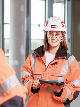 Foto von drei Personen in oranger Arbeitskleidung auf der Baustelle.