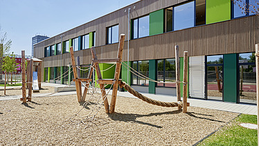 Photo of a wooden school from the outside. You can see the wooden building and the garden area.