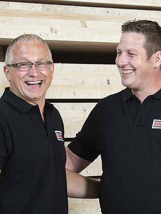 Photo of two men laughing. A stack of LENO plywood can be seen in the background.