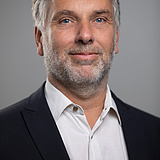 Photo of a smiling man with a grayish full beard, black jacket and white shirt. Martin Haller.