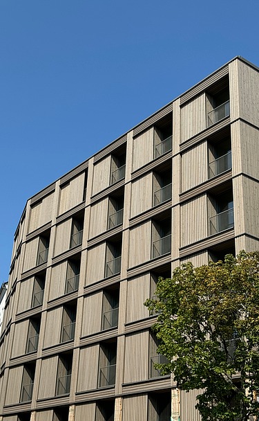 Foto der mehrgeschossigen Wohnanlage in der Stendaler Straße Berlin. Man sieht ein hohes Gebäude mit Holzfassade.