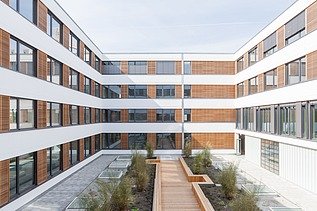 Photo of the Flexim Berlin office building from the outside. You can see a large U-shaped building made of wood with a wooden plaster façade and flat roof.