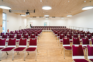 Photo of a lecture hall furnished with red chairs at Witten University. You can see a large wooden ceiling. 