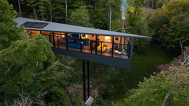 Photo of a wooden house on steel stilts in the middle of the forest.