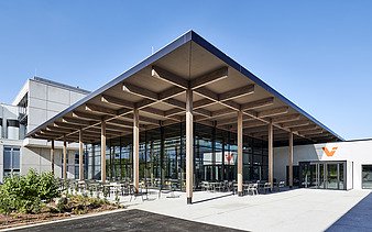 Außenaufnahme des Mitarbeiterrestaurants Viessmann in Allendorf: Zu sehen ist ein Gebäude mit vielen Glasflächen und Flachdach mit großem Holzvorsprung.